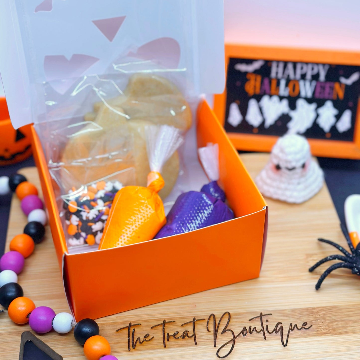 Halloween-themed treat box with candy on a wooden surface, featuring 'The Treat Boutique' branding.