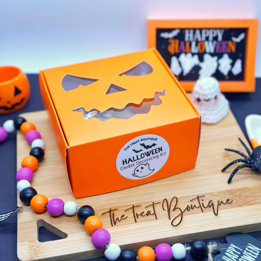 Orange Halloween-themed box with a jack-o'-lantern design on a wooden board with 'The Treat Boutique' branding.
