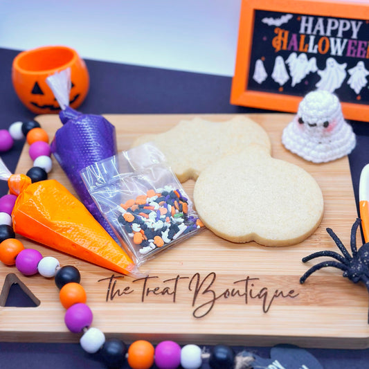 Halloween-themed treats and decorations on a wooden board with 'The Treat Boutique' branding.
