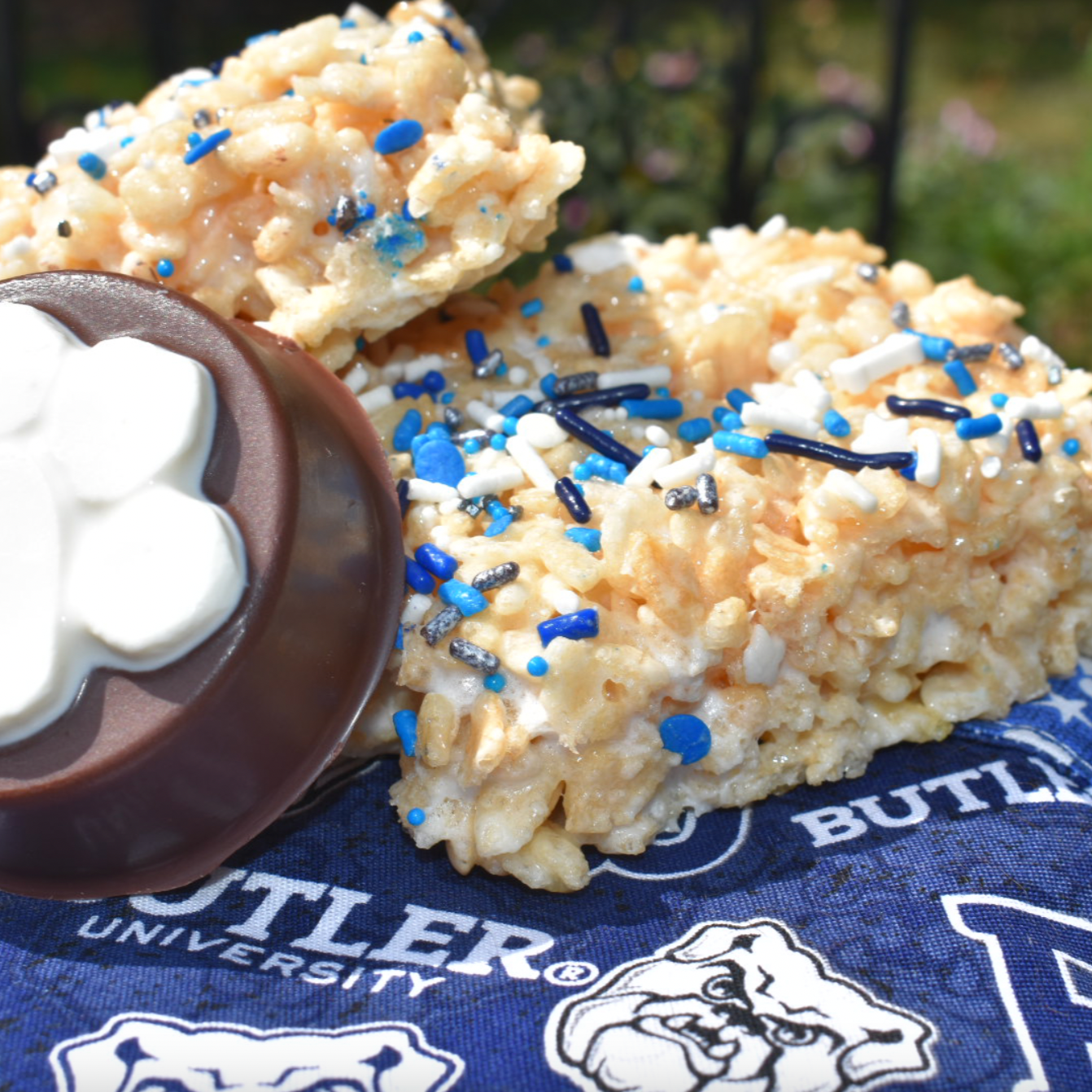 Two crispy rice treats with blue and white sprinkles and a chocolate on a blue Butler University towel.