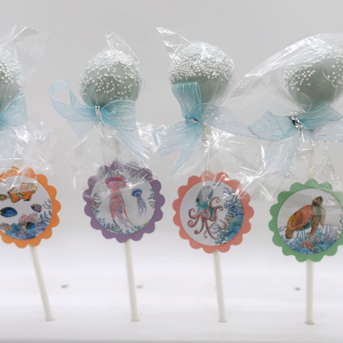 Four cake pops on sticks with decorative labels against a white background