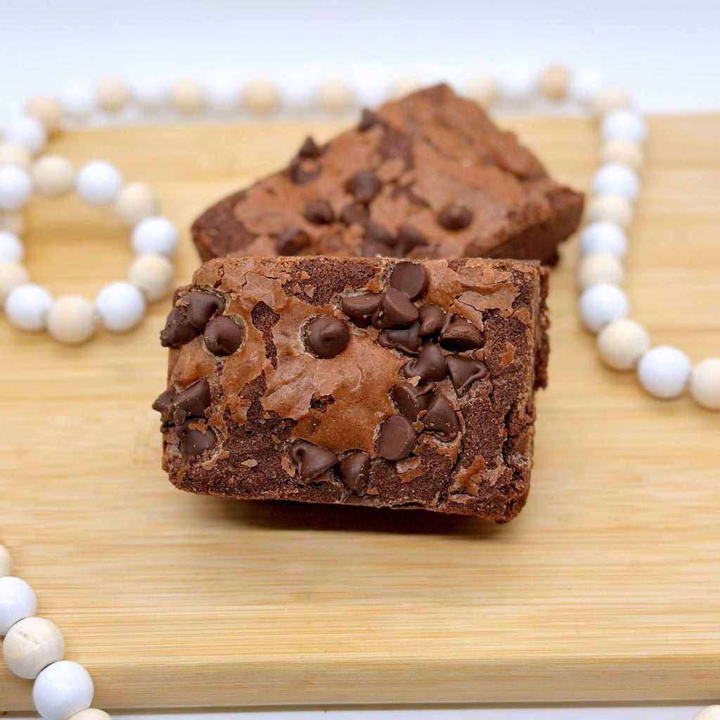 Chocolate brownies with chocolate chips on a wooden board, surrounded by a white beaded string.