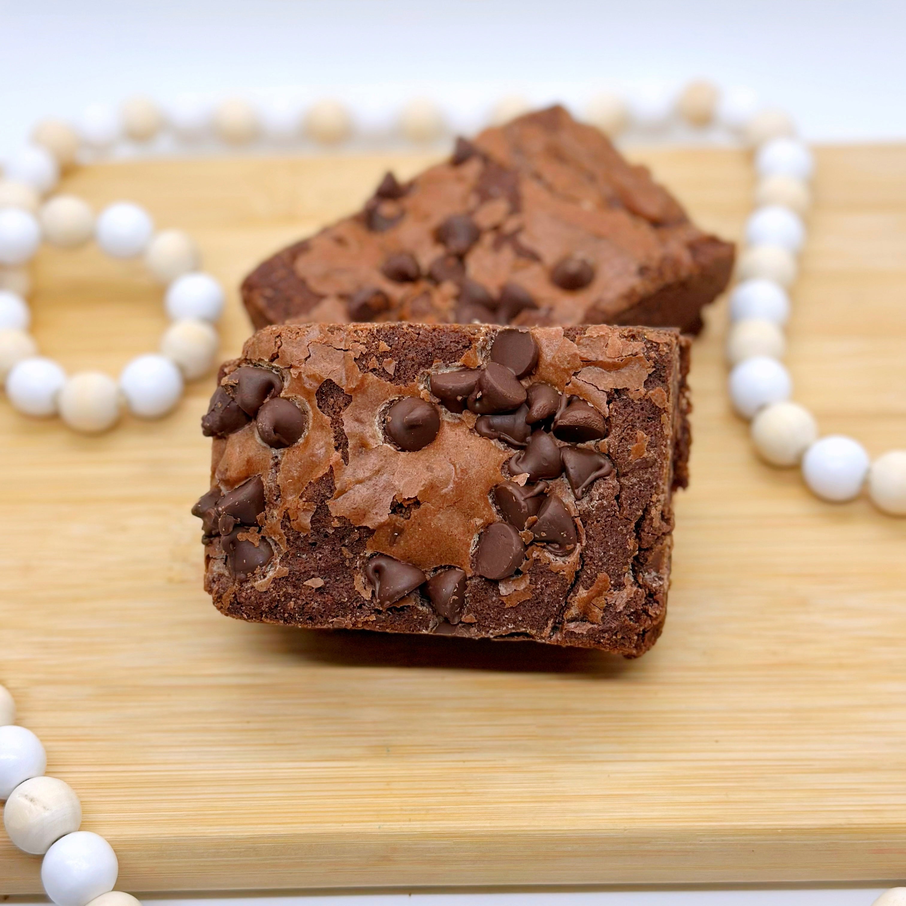 Chocolate brownies with chocolate chips on a wooden board, surrounded by a white beaded string.