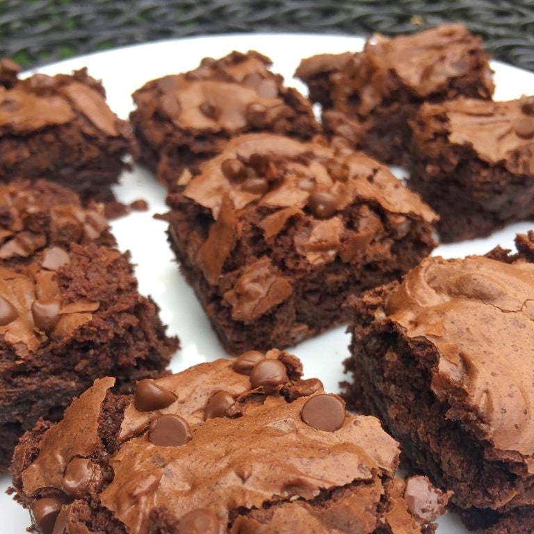 Multiple chocolate brownie pieces with chocolate chips on a white tray.