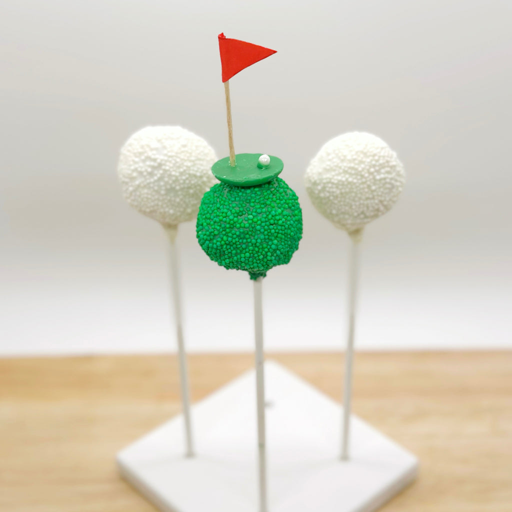 Golf-themed cake pops with a green glittery base and red flag on a white background