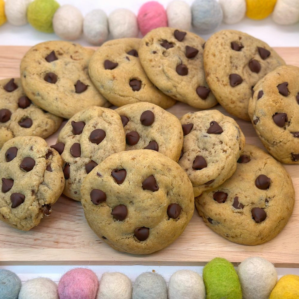 A top down angle of chocolate chip cookies on a wooden board with a colorful felt beaded string around it.