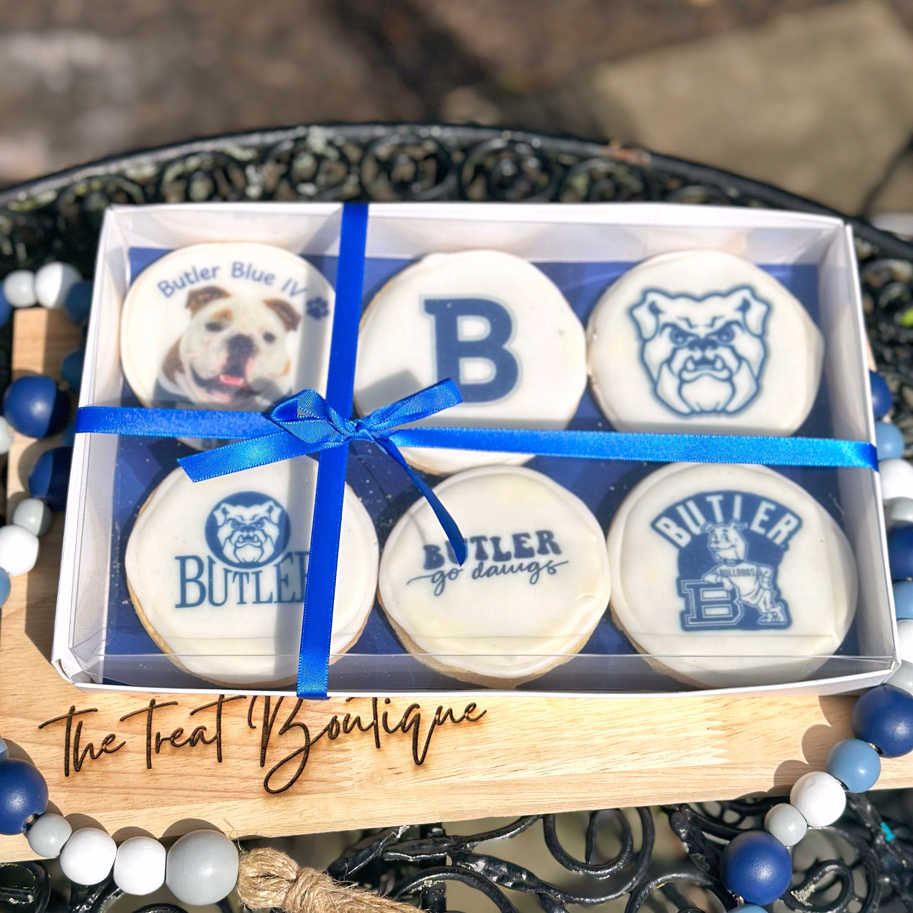 Box of Butler-themed cookies with blue ribbon on a decorative stand.