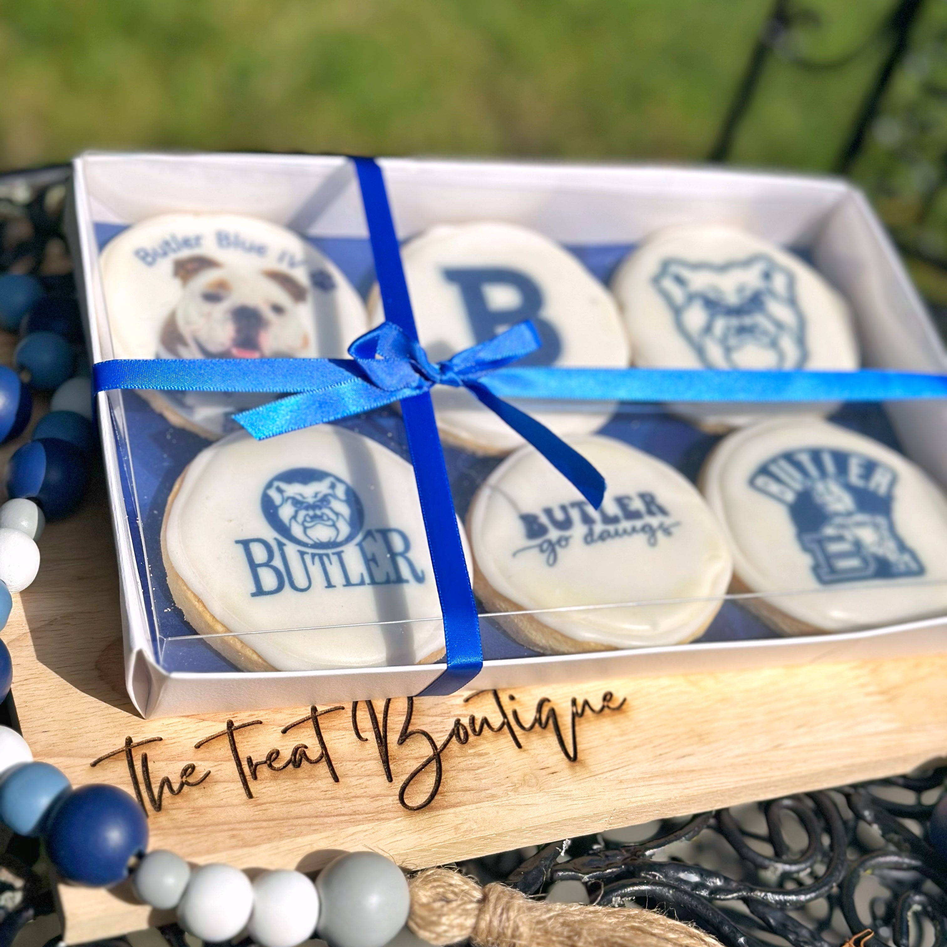 Box of cookies with blue ribbon and 'Butler' branding on a wooden tray with 'The Treat Boutique' branding.