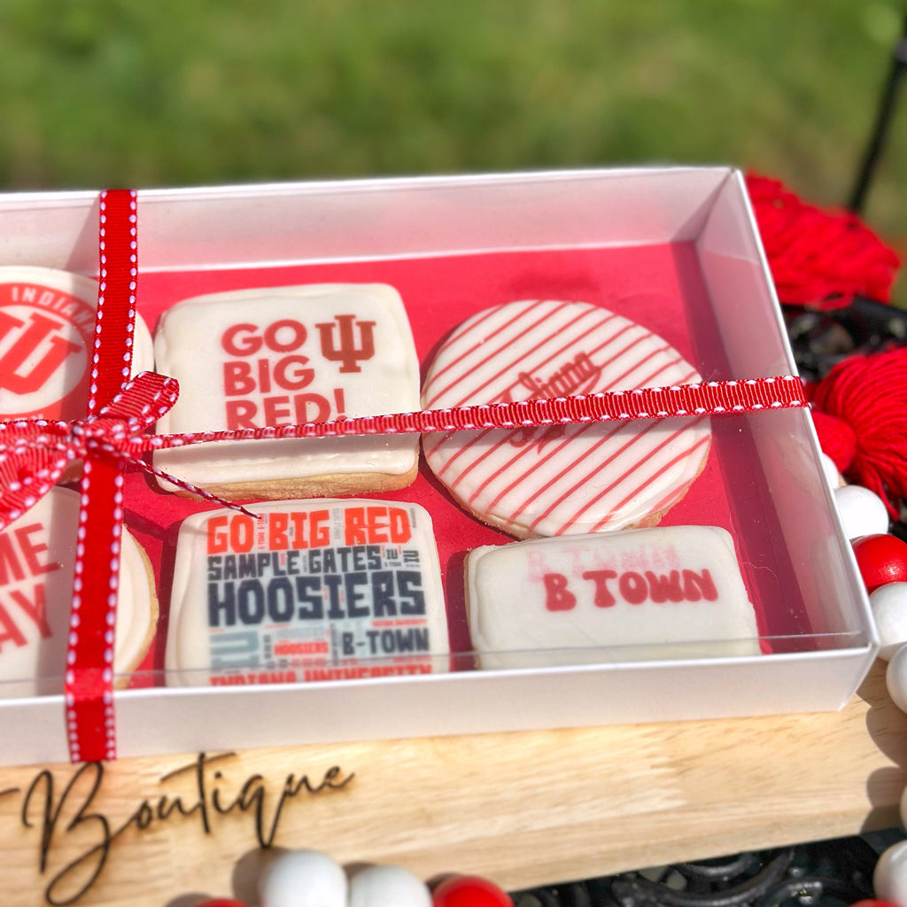 Close up of an IU themed cookie set with a red ribbon on a wooden stand, branded 'The Treat Boutique', with a blurred grass background.