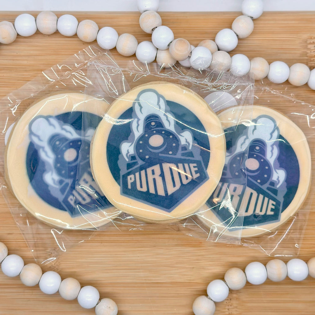 Three circle cookies with the Purdue logo printed on it in black and gold sit on a wooden tray with a wooden beaded string around it.