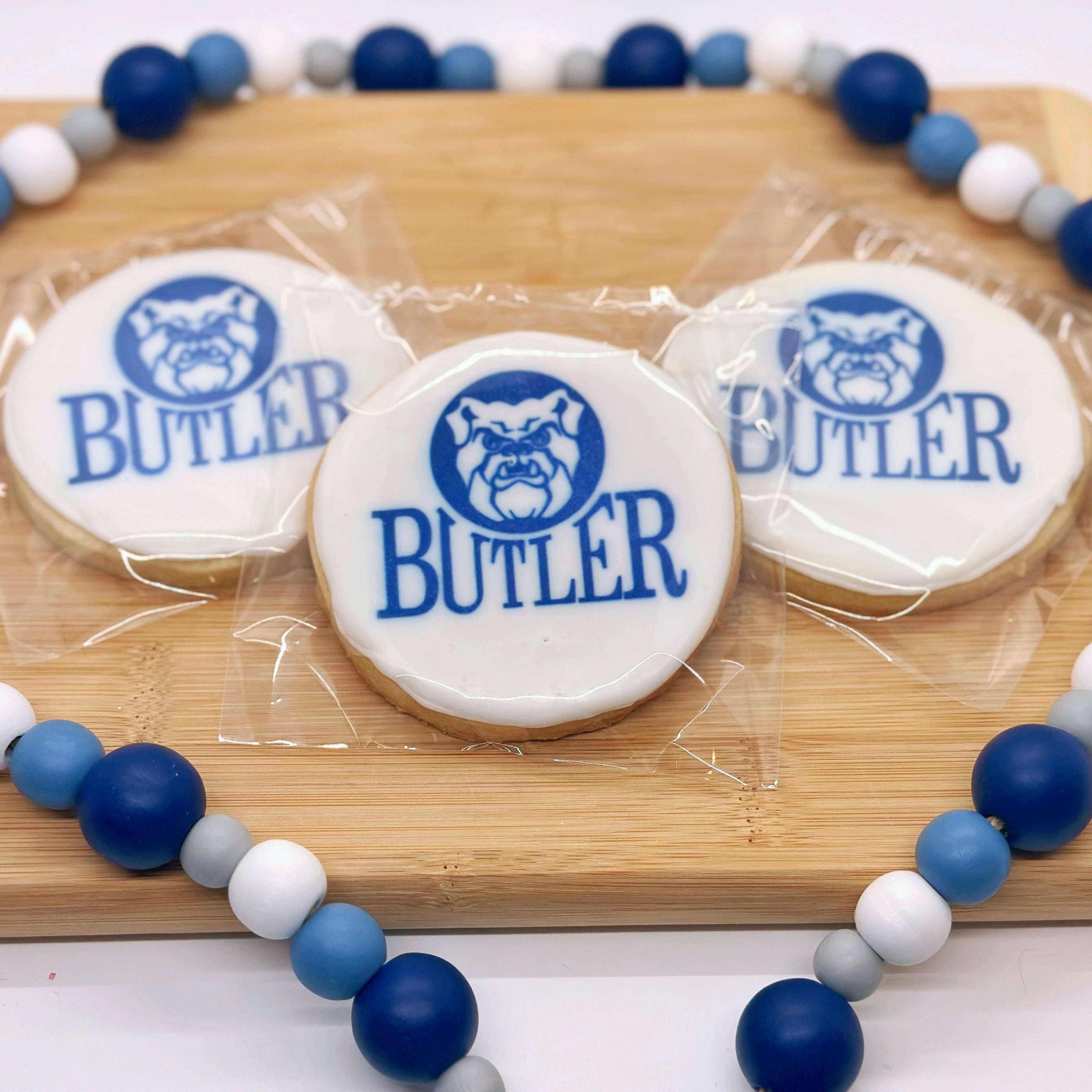 Three circle Butler cookies with blue and white design on a wooden board with blue and whtie decorative beads.
