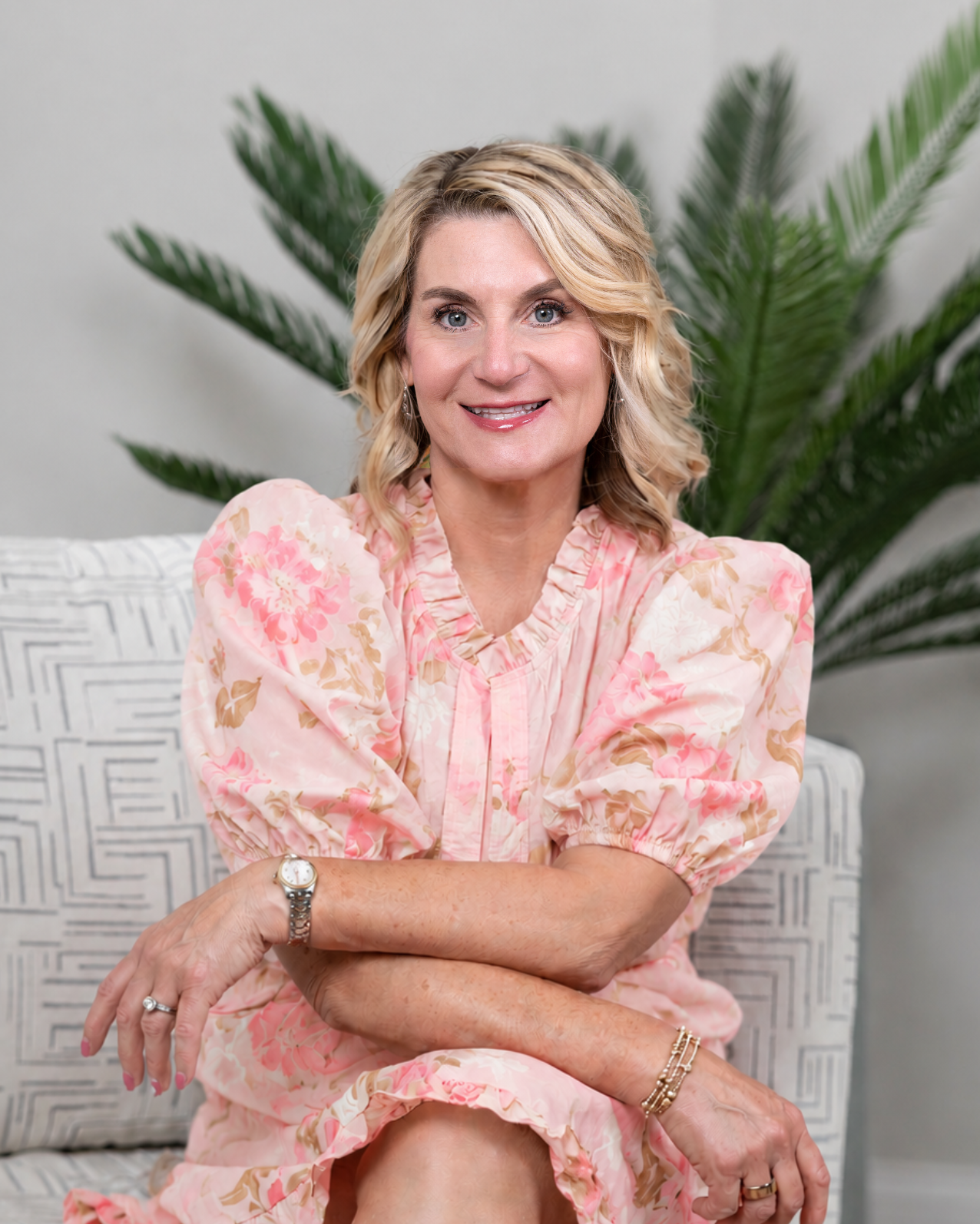 Woman in a pink floral dress sitting on a couch with a plant in the background